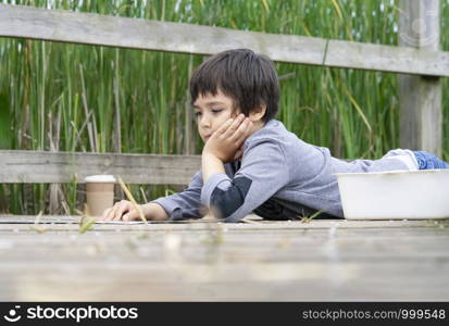 Outdoor portrait of happy boy lying on wooden bridge reading some thing on paper,Active child having fun playing in wildlife park,Kid having adventure in nature reserve in sunny day summer