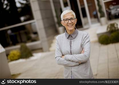 Outdoor portrait of happy cheerful senior businesswoman with crossed arms