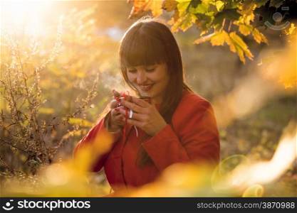 Outdoor portrait of happy woman drinking hot tea at autumn park