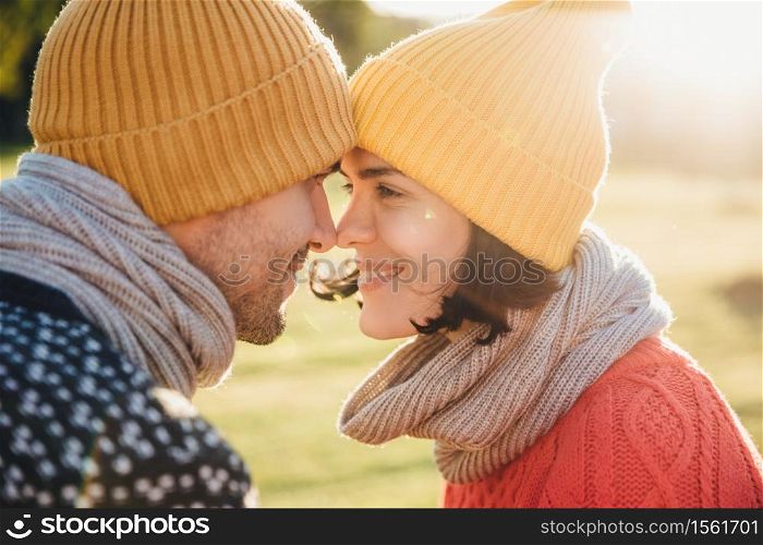 Outdoor portrait of lovely female and her boyfriend, look at each other`s eyes, keep noses together, enjoy calmness and togetherness. Handsome young man and his girlfriend have good time together