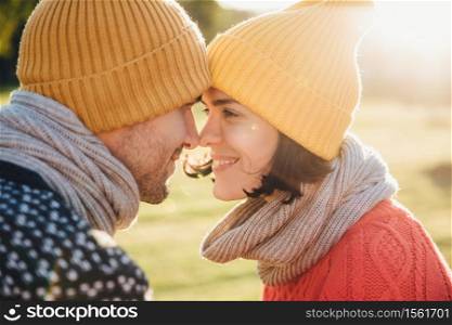 Outdoor portrait of lovely female and her boyfriend, look at each other`s eyes, keep noses together, enjoy calmness and togetherness. Handsome young man and his girlfriend have good time together