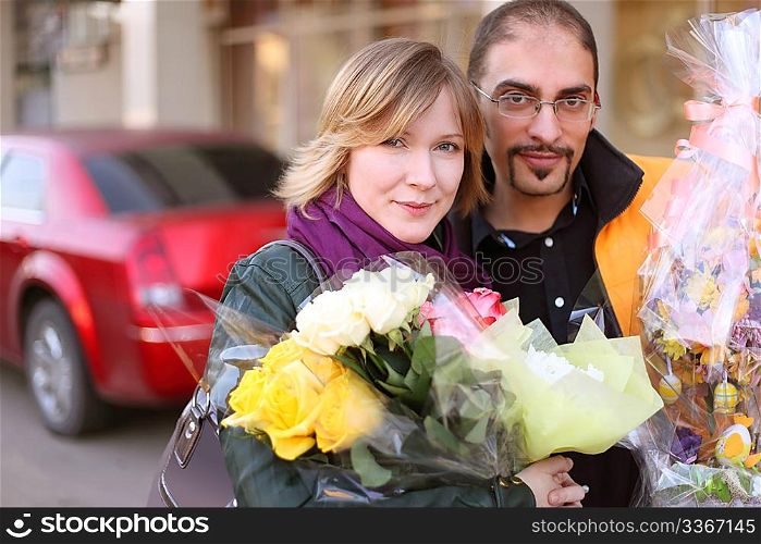 outdoor portrait of man in glasses and beauty blond girl with flower bouquets, looking at camera