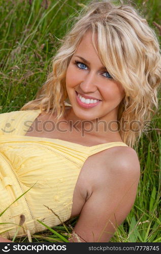 Outdoor portrait of smiling and happy, beautiful young female teenager with blonde hair and perfect teeth in a green field