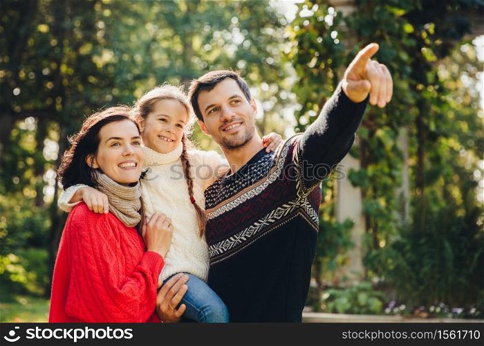 Outdoor portrait of smiling happy friendly family have walk together. Affectionate father shows his small daughter something into distance. Family admire sunrise, beautiful nature, wear warm clothes