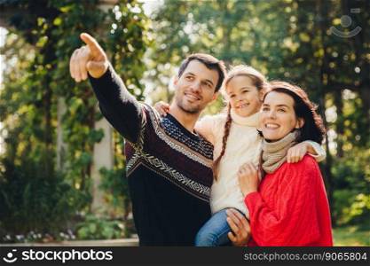 Outdoor portrait of smiling happy friendly family have walk together. Affectionate father shows his small daughter something into distance. Family admire sunrise, beautiful nature, wear warm clothes