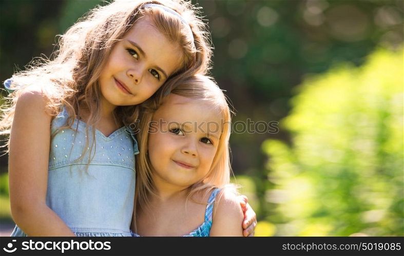 Outdoor portrait of two embracing cute little girls