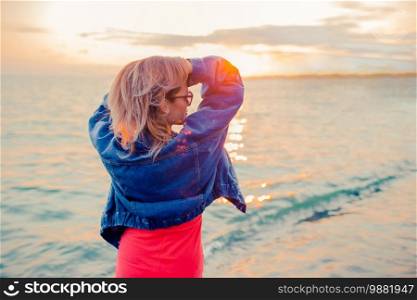 Outdoor portrait of woman in red dress on the beach at sunset. Outdoor fashion portrait of stylish girl wearing jeans jacket on the beach.