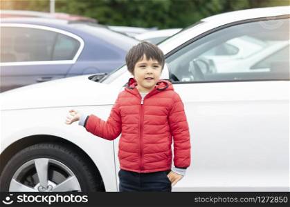 Outdoor portrait preschool kid boy with a smiling face standing next to the car, Happy childwith smiling face standing alone in car park in sunny day spring or summer.