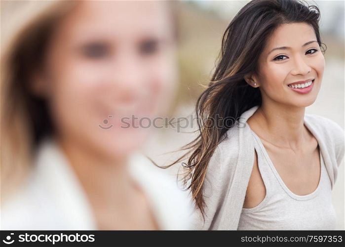 Outdoor profile portrait of a beautiful smiling happy Chinese Asian young woman or girl with blond female friend at beach