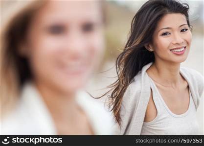 Outdoor profile portrait of a beautiful smiling happy Chinese Asian young woman or girl with blond female friend at beach