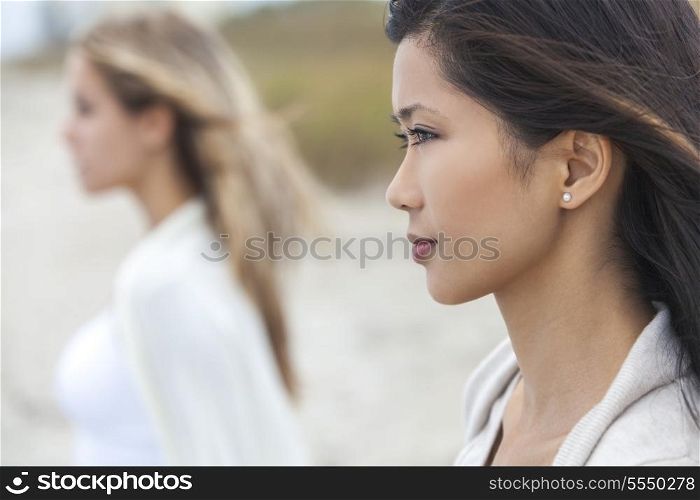 Outdoor profile portrait of a beautiful thoughtful Chinese Asian young woman or girl with blond female friend at beach