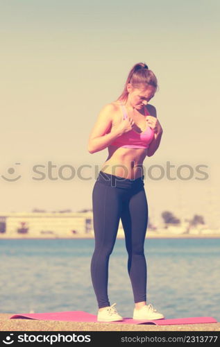 Outdoor relax, sport, fintess concept. Woman in sports suit standing on dyke next to sea stretching before workout.. Woman in sportswear standing on dyke by sea