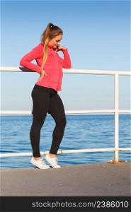 Outdoor relax, sport, fintess concept. Woman in sports suit standing on dyke next to sea resting after active workout.. Woman in sportswear standing on dyke by sea