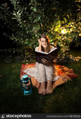 Outdoor shot at night of woman reading book at light of garden lantern