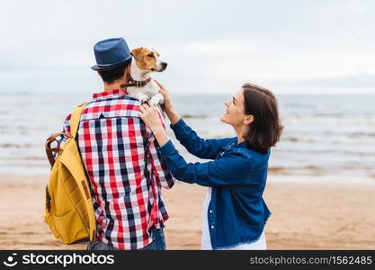 Outdoor shot of friendly family and their favourite dog come to sea to make photos and enjoy or breath fresh marine air, stand close to each other. People, holidays, recreation and leisure concept