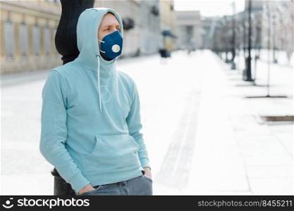 Outdoor shot of hipster wears sweatshirt and respiratory mask, walks in epidemic city, prevents virus, infection and coronavirus, afraids of being infected. Qaurantine time. Health safety concept