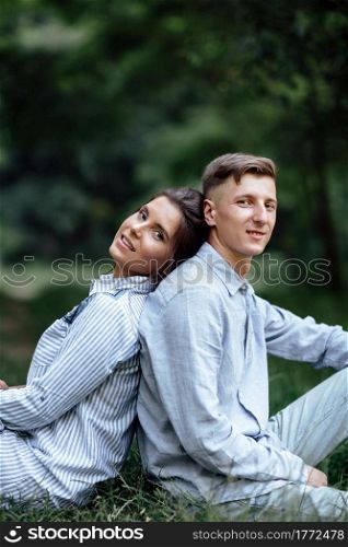 Outdoor shot of young happy couple in love sitting on grass on nature. Man and woman hugging, sunlight in summer park. Happy family in the evening sun light. The concept holiday. Outdoor shot of young happy couple in love sitting on grass on nature. Man and woman hugging, sunlight in summer park. Happy family in the evening sun light. The concept holiday.