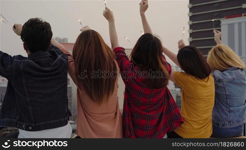Outdoor shot of young people at rooftop party. Happy group of asian friends enjoy and play sparkler at roof top party at evening sunset. Holiday celebration festive party. Teenage lifestyle party.