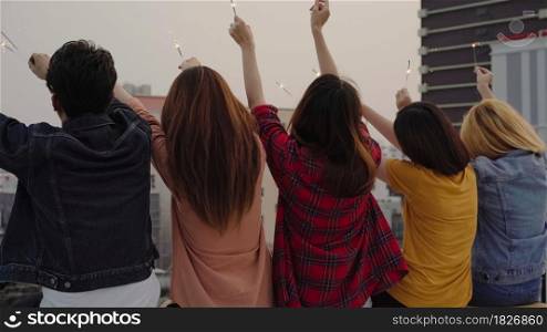 Outdoor shot of young people at rooftop party. Happy group of asian friends enjoy and play sparkler at roof top party at evening sunset. Holiday celebration festive party. Teenage lifestyle party.