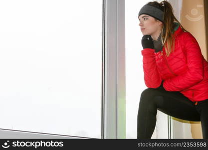 Outdoor sport exercises, sporty outfit ideas. Woman wearing warm sportswear getting ready before exercising looking throught window at home.. Woman wearing warm sportswear at home