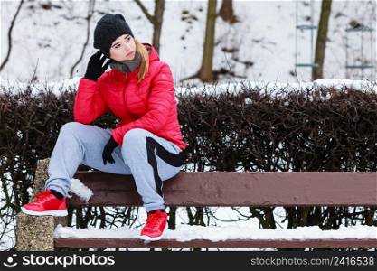 Outdoor sport exercises, sporty outfit ideas. Woman wearing warm sportswear getting ready before exercising, sitting on bench outside during winter.. Woman wearing sportswear sitting outside during winter