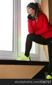 Outdoor sport exercises, sporty outfit ideas. Woman wearing warm sportswear getting ready before exercising looking throught window at home.. Woman wearing warm sportswear at home