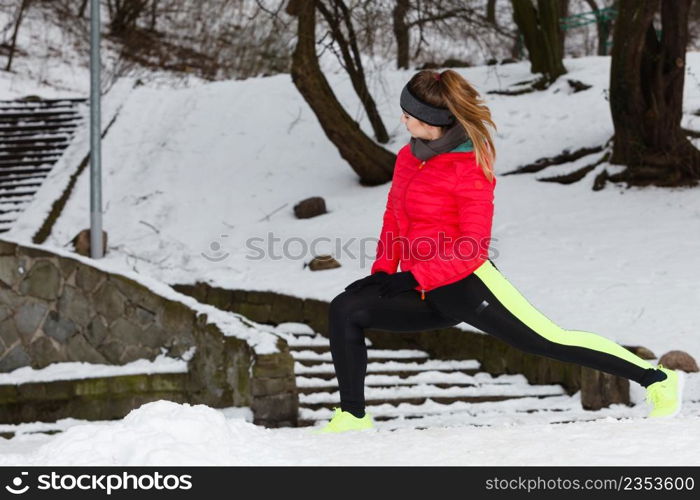 Outdoor sport exercises, sporty outfit ideas. Woman wearing warm sportswear training exercising stretching legs outside during winter.. Woman exercising legs outside during winter