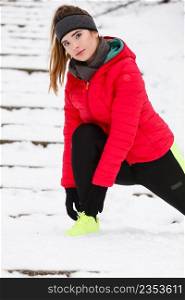 Outdoor sport exercises, sporty outfit ideas. Woman wearing warm sportswear training exercising stretching legs outside during winter.. Woman exercising legs outside during winter