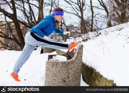 Outdoor sport exercises, sporty outfit ideas. Woman wearing warm sportswear training exercising stretching legs outside during winter.. Woman wearing sportswear exercising outside during winter