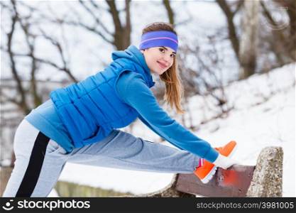 Outdoor sport exercises, sporty outfit ideas. Woman wearing warm sportswear training exercising stretching legs outside during winter.. Woman wearing sportswear exercising outside during winter