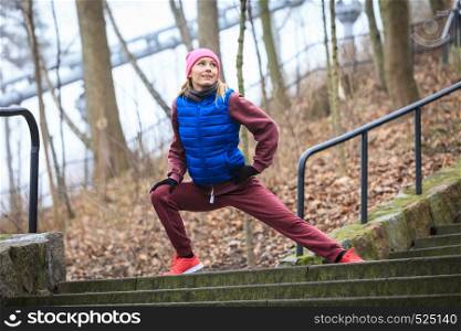 Outdoor sport exercises, sporty outfit ideas. Woman wearing warm sportswear training exercising, stretching legs outside during autumn.. Woman wearing sportswear exercising outside during autumn