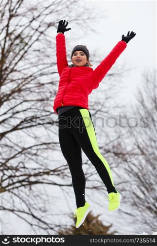 Outdoor sport exercises, sporty outfit ideas. Woman wearing warm sportswear training exercising outside during winter jumping out of joy. Woman wearing sportswear jumping