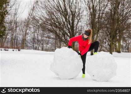 Outdoor sport exercises, sporty outfit ideas. Woman wearing warm sportswear training exercising outside during winter. Having fun while making snowman. Woman wearing sportswear exercising during winter