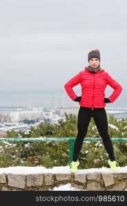 Outdoor sport exercises, sporty outfit ideas. Woman wearing warm sportswear training exercising outside during winter. Cityscape panorama in background. Woman wearing sportswear exercising during winter