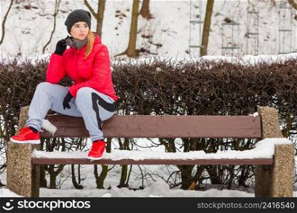 Outdoor sport exercising, sporty outfit ideas. Woman wearing warm sportswear relaxing after exercising sitting on bench outside during winter.. Woman wearing warm sportswear relaxing after exercising