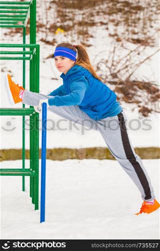 Outdoor sport exercising, sporty outfit ideas. Woman wearing warm sportswear training exercising stretching legs outside during winter.. Woman wearing sportswear exercising outside during winter