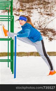 Outdoor sport exercising, sporty outfit ideas. Woman wearing warm sportswear training exercising stretching legs outside during winter.. Woman wearing sportswear exercising outside during winter
