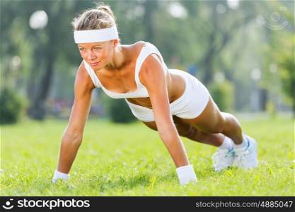 Outdoor workout. Young attractive sport girl in park doing push ups