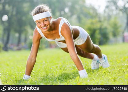 Outdoor workout. Young attractive sport girl in park doing push ups