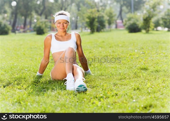 Outdoor workout. Young attractive sport girl in park sitting on grass