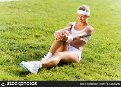 Outdoor workout. Young attractive sport girl in park sitting on grass