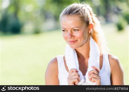 Outdoor workout. Young attractive sport girl in park with towel on neck