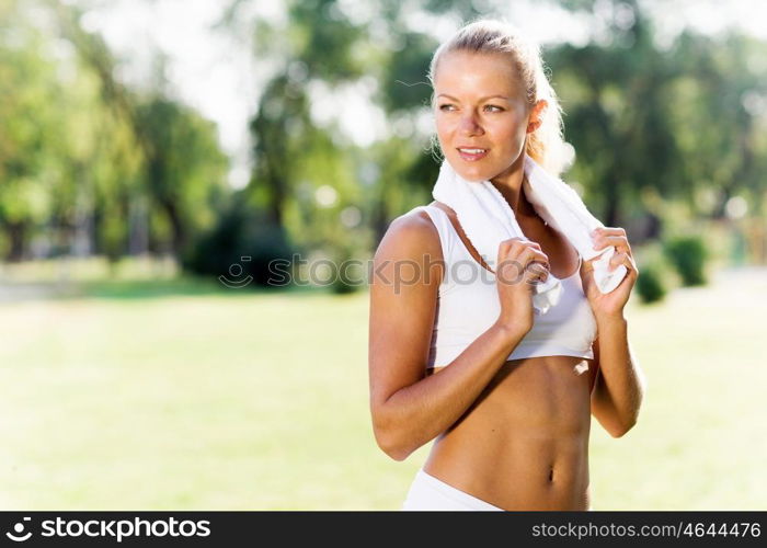 Outdoor workout. Young attractive sport girl in park with towel on neck