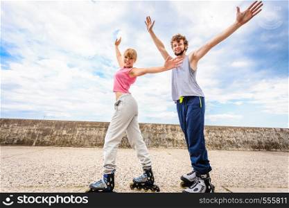 Outdoors activities sport and hobby. Exercises for healthy and strong body. Friends stretch together have fun riding rollerblades stand with outstretched arms.. Two people on rollerblades with spread arms.