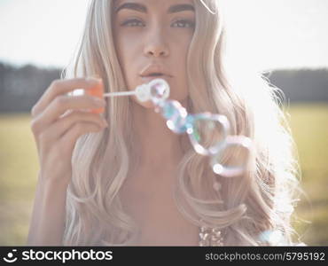 Outdoors fashion photo of beautiful blonde blowing bubbles