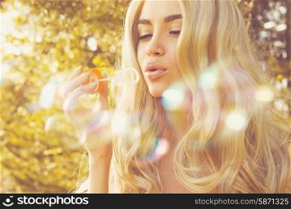 Outdoors fashion photo of beautiful blonde blowing bubbles