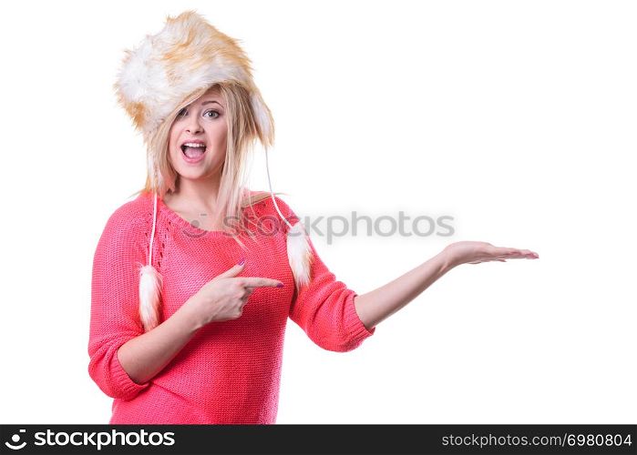 Outfit for cold days ideas, fashion and clothing concept. Attractive smiling blonde woman wearing furry winter hat presenting something on palm hand. Attractive woman wearing furry winter hat