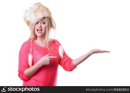 Outfit for cold days ideas, fashion and clothing concept. Attractive smiling blonde woman wearing furry winter hat presenting something on palm hand. Attractive woman wearing furry winter hat