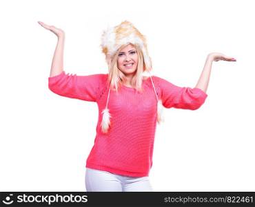 Outfit for cold days ideas, fashion and clothing concept. Attractive smiling blonde woman wearing furry winter hat presenting something on palm hands. Attractive woman wearing furry winter hat