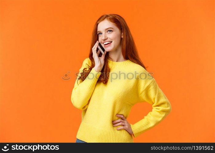 Outgoing pretty redhead girl having conversation on phone, calling friend, making arrangements, woman booking hotel or trip using mobile, speaking via smartphone, standing orange background.. Outgoing pretty redhead girl having conversation on phone, calling friend, making arrangements, woman booking hotel or trip using mobile, speaking via smartphone, standing orange background